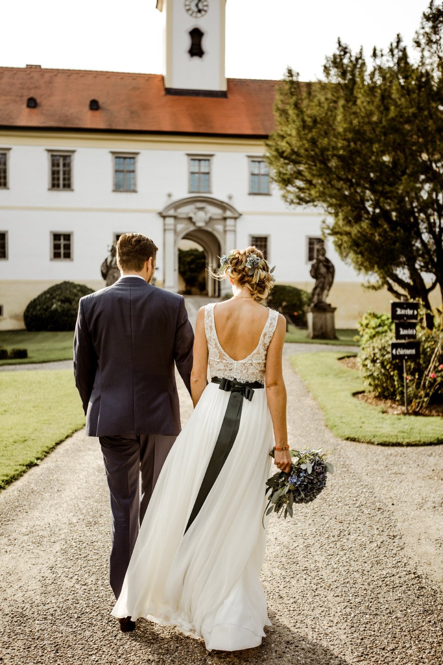 Braut und Bräutigam laufen Weg im Schloss Altenhof entlang