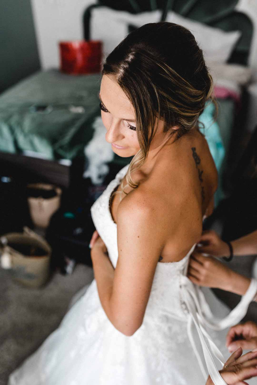 Braut bekommt Brautkleid zugeknöpft