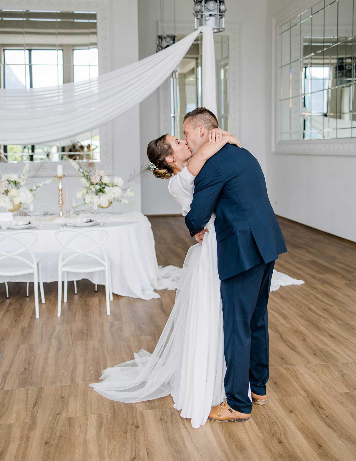 Küssendes Brautpaar vor dem eingedeckten Hochzeitstisch